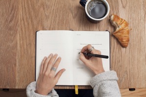 person writing in notebook with coffee and croissant